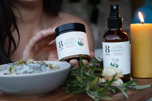 Eco-friendly beauty products featuring a calming body butter and ritual spray with lavender and chamomile, displayed with herbs and a candle.